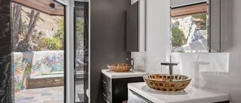 Un baño moderno con un ventanal grande, dos lavamanos con cuencos decorativos y un mueble oscuro.