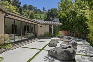 Una casa moderna con un patio, mobiliario exterior y un ventanal grande con vistas a un jardín.