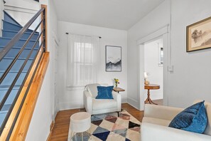 Stylish living space with a staircase, armchair, and artwork, set against a backdrop of sheer curtains and a patterned rug.