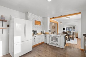Contemporary kitchen with brick accent wall, wooden flooring, and wooden beam ceiling, featuring a refrigerator, oven, and sink.