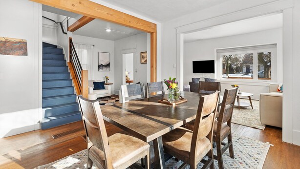 Un comedor espacioso con una gran mesa de madera y sillas, una escalera con escalones azules, y vistas al exterior a través de una ventana.