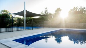 A swimming pool with a shaded area and a fence. - Bellevue Holiday House (Moore Creek)