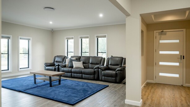 A modern living room with a leather sofa, a coffee table, and a blue rug. There are large windows and a door with a light fixture. - Bellevue Holiday House (Moore Creek)