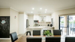 A modern kitchen with white cabinets, a central island, and a dining area with a wooden table and black chairs. - Bellevue Holiday House (Moore Creek)
