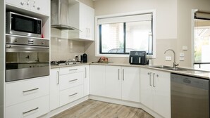 A modern kitchen with white cabinets, stainless steel appliances, a window, and a dishwasher. - Bellevue Holiday House (Moore Creek)