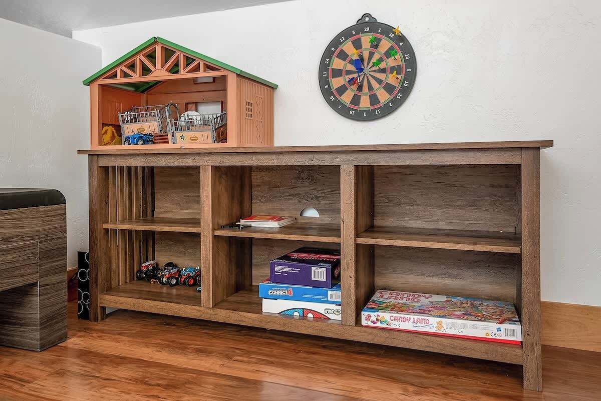 A wooden shelf unit with compartments, a dartboard, and a toy train set on top.