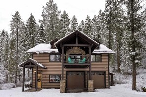 A two-story lodge with a stone facade, a balcony with chairs, and a snow-covered roof.