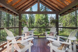 Een overdekt terras met Adirondack stoelen en uitzicht op een bebost gebied.
