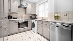 A modern kitchen with stainless steel appliances, a built-in oven, microwave, and dishwasher, and a window with blinds. - Modern 2 Bedroom Apartment - Jewellery Quarter - Pet Friendly (Birmingham)
