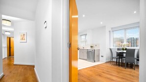A modern kitchen with white cabinets, a dishwasher, and a dining area with a table and chairs. - Modern 2 Bedroom Apartment - Jewellery Quarter - Pet Friendly (Birmingham)
