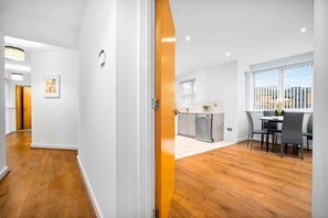 A modern kitchen with white cabinets, a dishwasher, and a dining area with a table and chairs. - Modern 2 Bedroom Apartment - Jewellery Quarter - Pet Friendly (Birmingham)