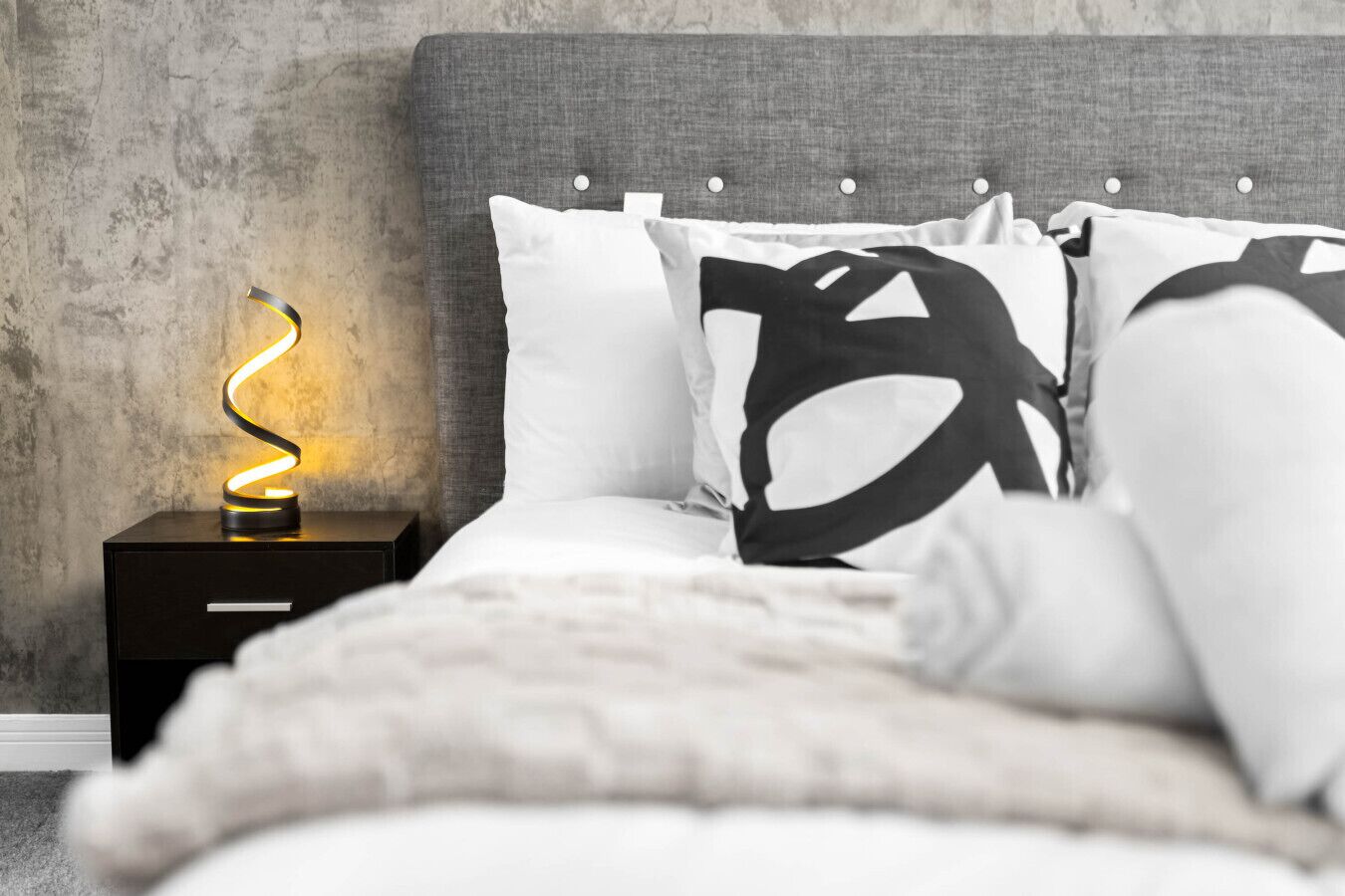 Quarto com cama, almofadas, mesa de cabeceira e abajur.