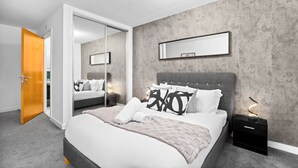A modern bedroom with a large bed, a nightstand, a mirror, and a door leading to another room. - Modern 2 Bedroom Apartment - Jewellery Quarter - Pet Friendly (Birmingham)