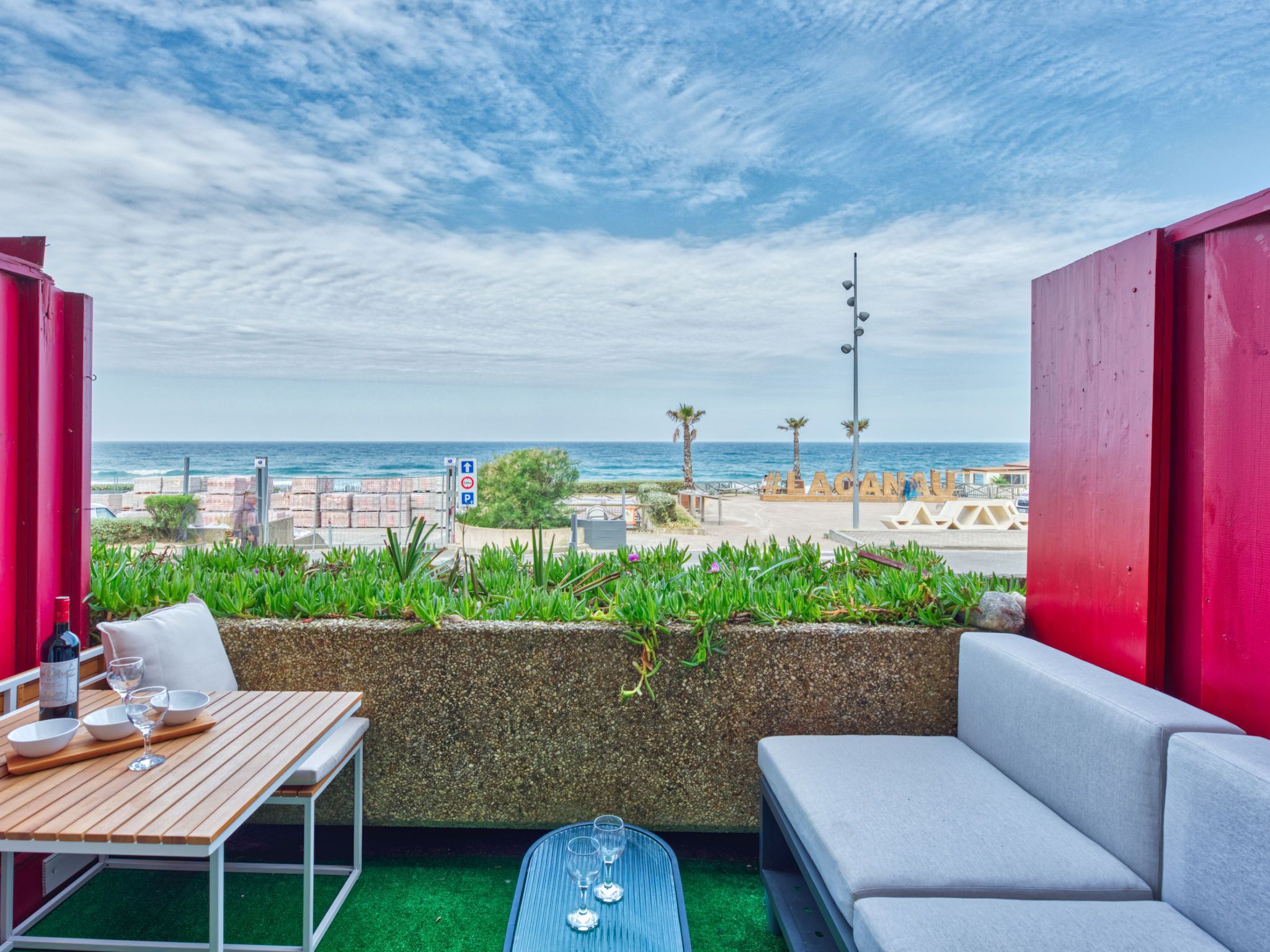 Ein Balkon mit Blick auf den Strand, ein Tisch mit Gläsern und ein Sofa.