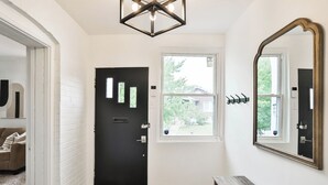 Un pasillo con una puerta negra, una ventana, un espejo y un banco de madera.