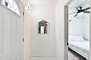 A narrow hallway with a white door, a small mirror, and a ceiling fan in a bedroom.