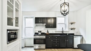 Una cocina moderna con armarios negros, horno de acero inoxidable, lavavajillas empotrado y una mesa de comedor negra.