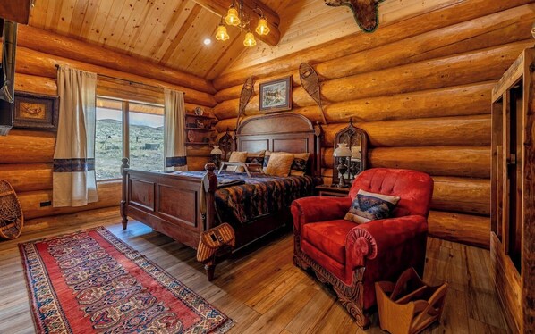 Un dormitorio tipo cabaña de madera con una cama de madera, un sillón rojo, una alfombra grande y vistas al exterior.