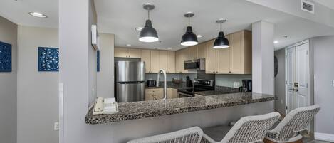 Cozinha moderna com bancadas de granito, eletrodomésticos de aço inoxidável e banquetas.