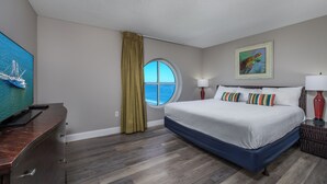 Une chambre d’hôtel avec un grand lit, une télévision, une fenêtre avec des rideaux et un tableau au mur.