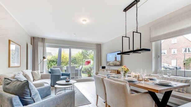 A modern living room with a sofa, chairs, a dining table set for six, and a TV mounted on the wall.