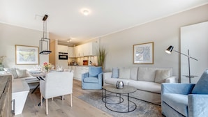 A modern living room with a sofa, armchairs, a coffee table, and a dining area with a table set for four.