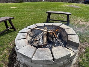 Een ronde vuurkuil van steen met een houten bank aan de ene kant en een picknicktafel aan de andere, gelegen in een grasrijke omgeving.