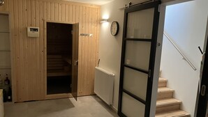 Un couloir avec une porte en bois donnant sur un escalier, une horloge murale et un thermostat.