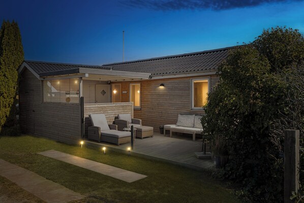 Une maison moderne dotée d’un patio couvert, d’un espace salon extérieur et d’une pelouse bien entretenue.