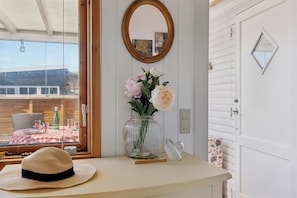 Une piĂšce avec une fenĂȘtre, un vase rempli de fleurs, un chapeau, un miroir et une porte.