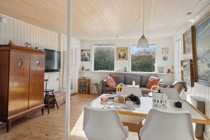 A cozy room with a wooden cabinet, a dining table with chairs, a sofa, and a large window.