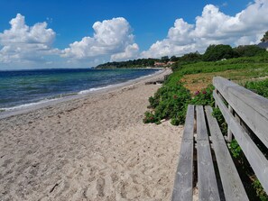 A beach with a wooden bench, clear blue sky, and calm sea.