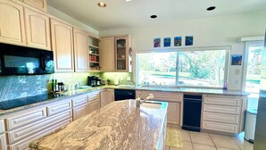 A kitchen with granite countertops, white cabinetry, a built-in microwave, and a window providing a view of the outdoors.