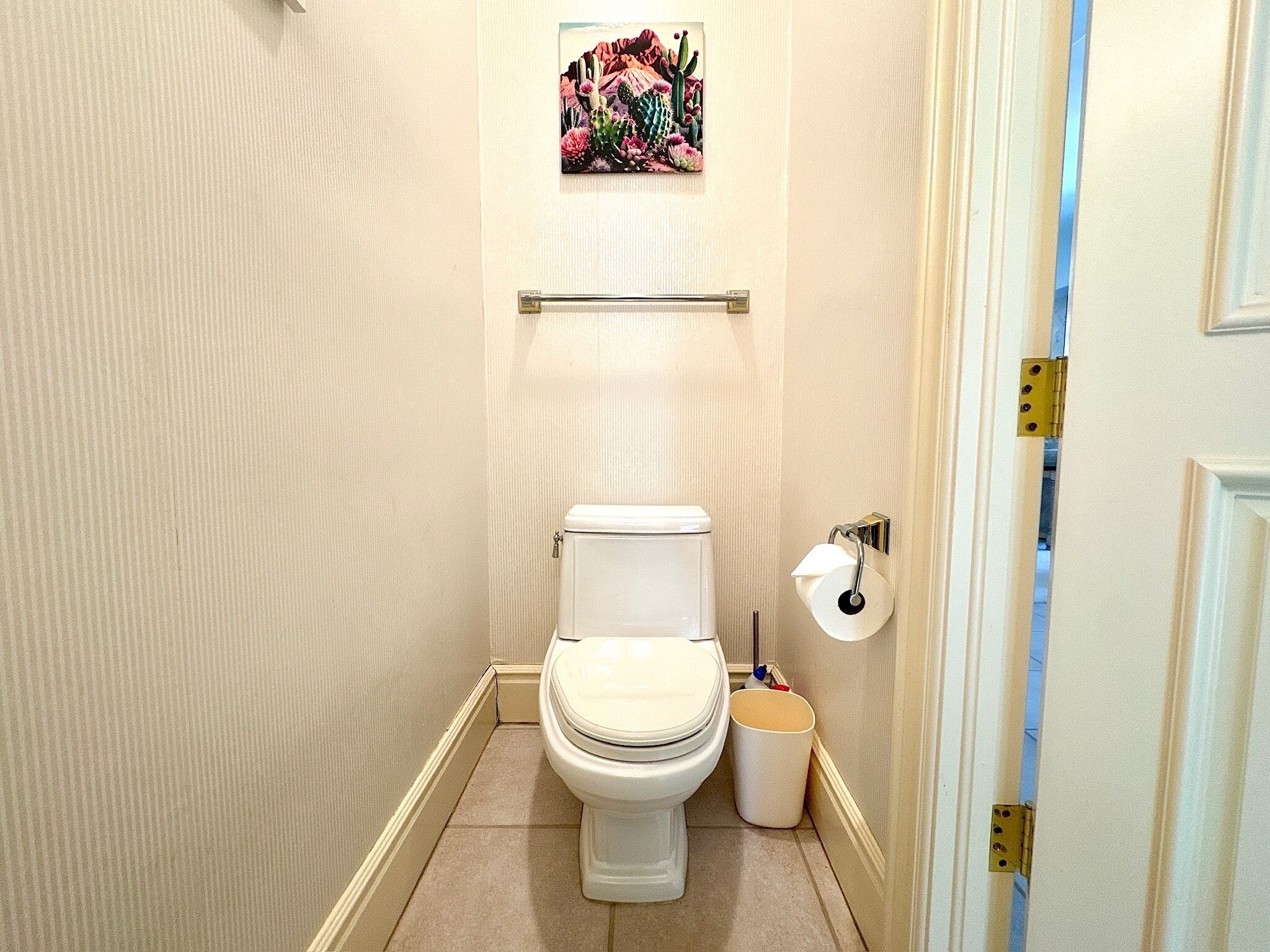 A small, narrow bathroom with a toilet, a roll of toilet paper, and a trash bin.