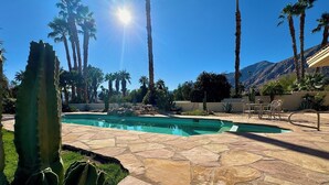 A pool area with stone flooring, palm trees, and a cactus in the foreground.