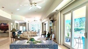 A spacious living room with a large blue marble coffee table, beige sofas, and a dining area with chairs.