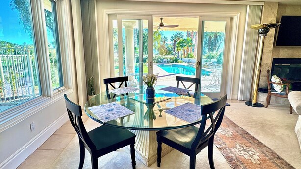 A glass-top dining table with four chairs, a view of a swimming pool, and a fireplace.