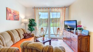Ein Wohnzimmer mit einer Couch, einem Fernseher, einer Pflanze und Blick durch eine Glastür.
