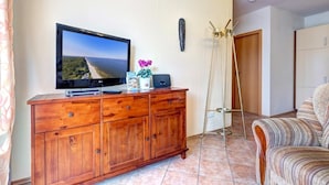 Ein Zimmer mit einem Holzkabinett, einem Flachbildfernseher, einer Pflanze, einer Leiter und einem gestreiften Sofa.