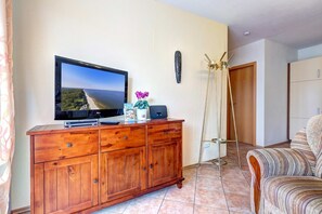 A room with a wooden cabinet, a flat-screen TV, a plant, a ladder, and a striped sofa.