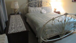 A bedroom with a metal bed frame, a bedside table with a lamp, and a window with curtains.