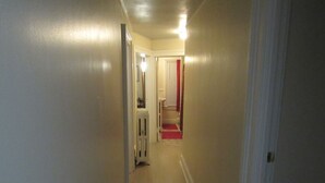 A narrow hallway with a light fixture on the ceiling, a radiator, and a red carpet leading to a door.