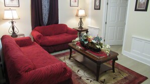A living room with two red sofas, a coffee table with flowers, and a door in the background.