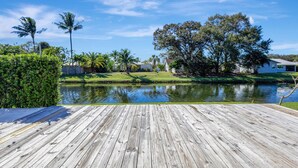 Una terraza de madera que conduce a una masa de agua tranquila, con un césped y árboles al fondo.