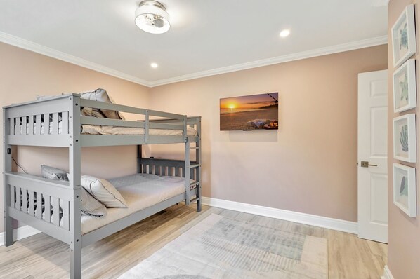 Una cama litera en una habitación con pared color beige, un cuadro con un atardecer enmarcado y una puerta decorada con marcos de fotos.