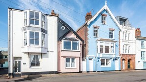 Une rangée de maisons aux couleurs vives, chacune présentant un style architectural distinct, notamment un bâtiment blanc doté d’une baie vitrée et une maison rose avec un toit en pente.