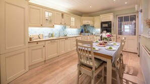 Une cuisine spacieuse, dotée de meubles de couleur claire, d’un îlot central et d’un coin repas avec une table dressée pour quatre personnes.