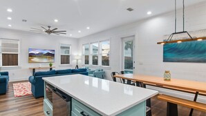 Una cocina moderna con una isla central, un comedor con mesa de madera y una sala de estar con sofás azules.
