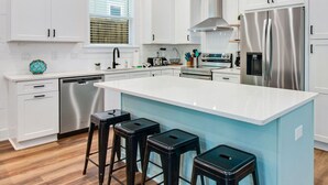 Una cocina moderna con armarios blancos, electrodomésticos de acero inoxidable y una isla central con taburetes.