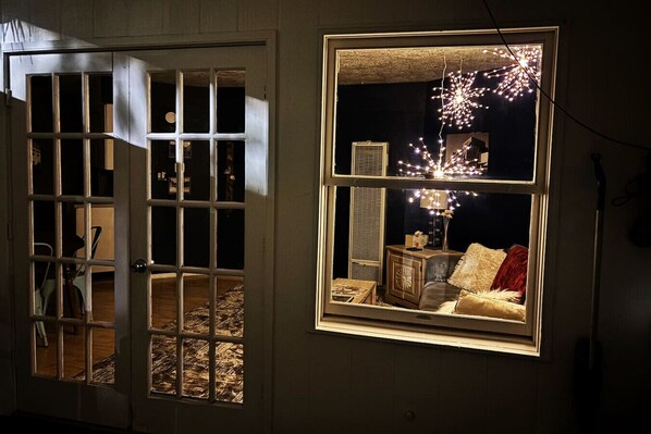 A room with a large window, a door, and a visible interior including a sofa and a lamp.